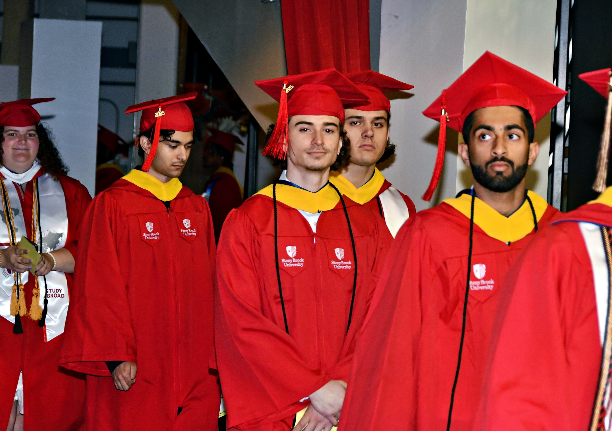 Stony Brook University College of Business Graduates in red caps and gowns standing together and smiling