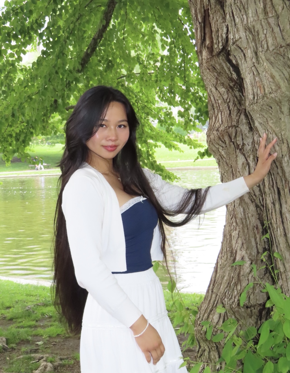 Person smiling and standing with their hand on a tree