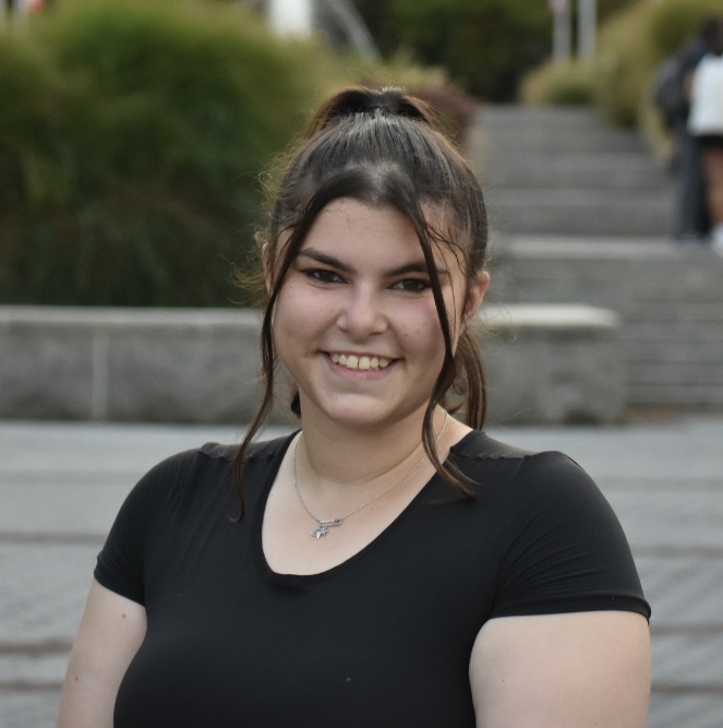 A smiling person stands in front of a fountain outdoors
