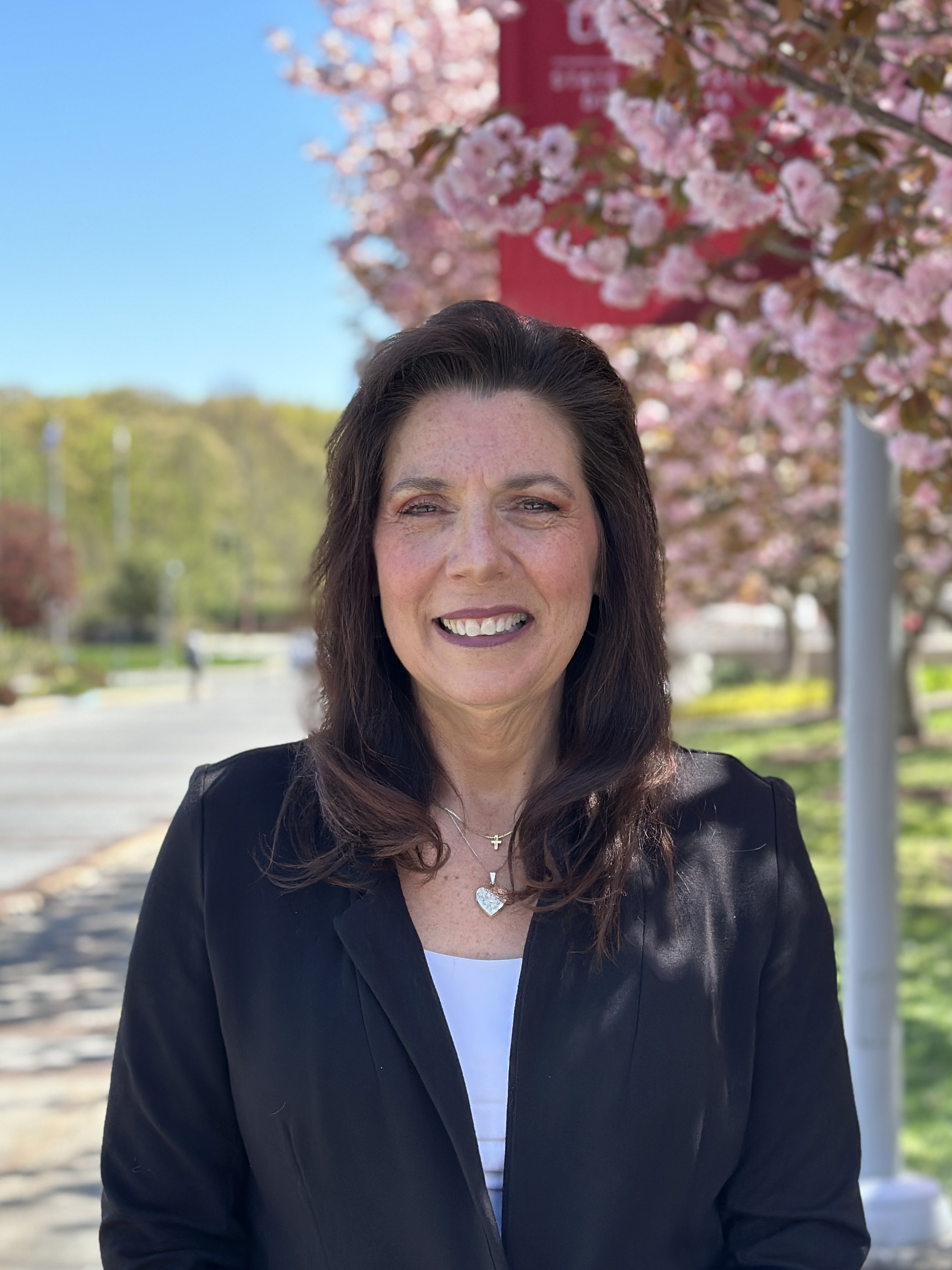 A smiling person stands outdoors in front of a cherry blossom tree
