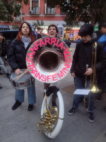 Three musicians playing in a street band, with a drum, a large horn, and a trombone.