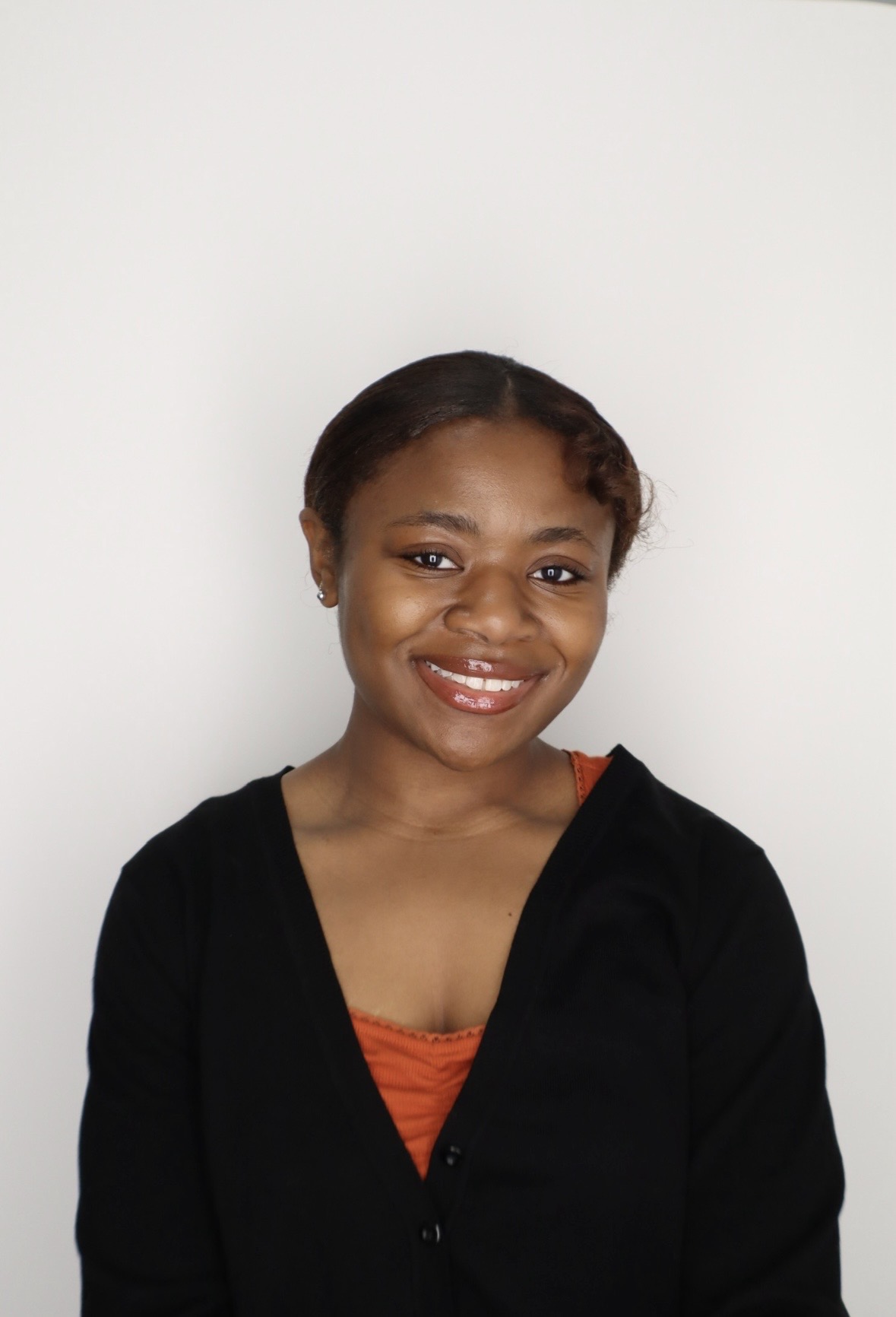 Smiling woman in a black cardigan over an orange top against a plain white background. She exudes a warm, friendly vibe.