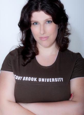 A headshot of a woman with dark, wavy hair and blue eyes, looking directly at the camera with a neutral expression. She is wearing a dark brown t-shirt that has the text "STONY BROOK UNIVERSITY" printed across the chest in white capital letters. The background is a plain, solid white.